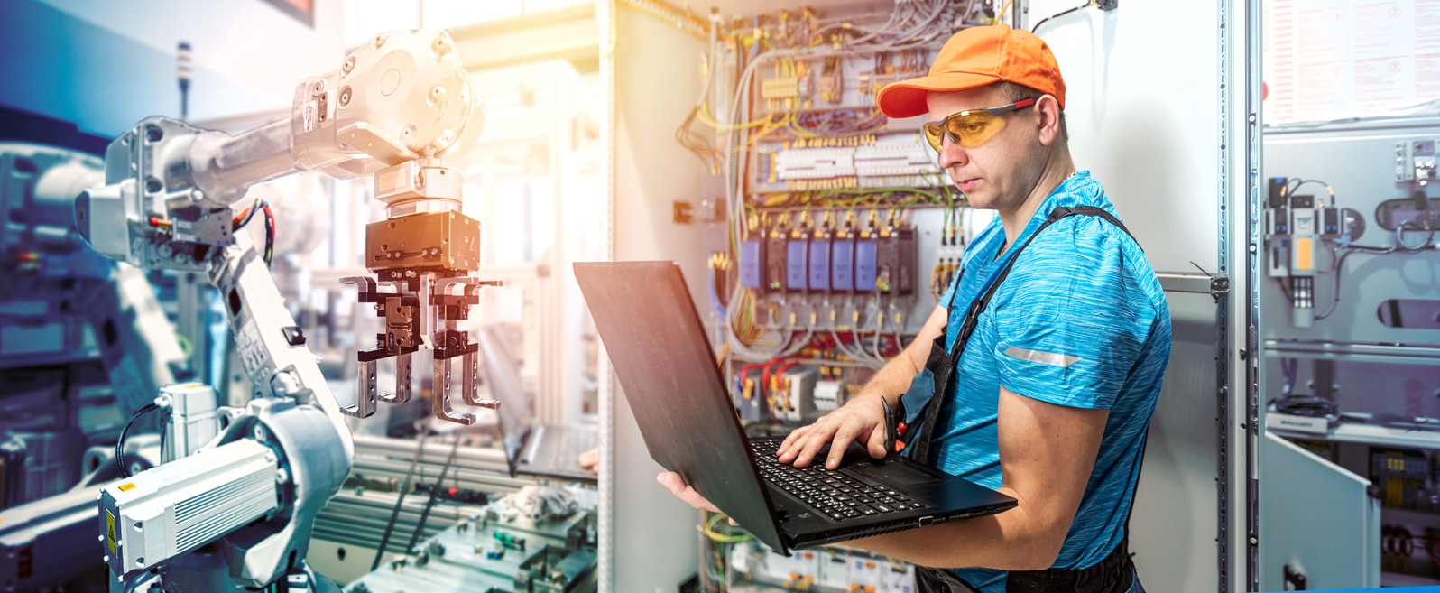 The electrician works with a laptop during programming of machines in the electrical production factory. Work in electrical industry.